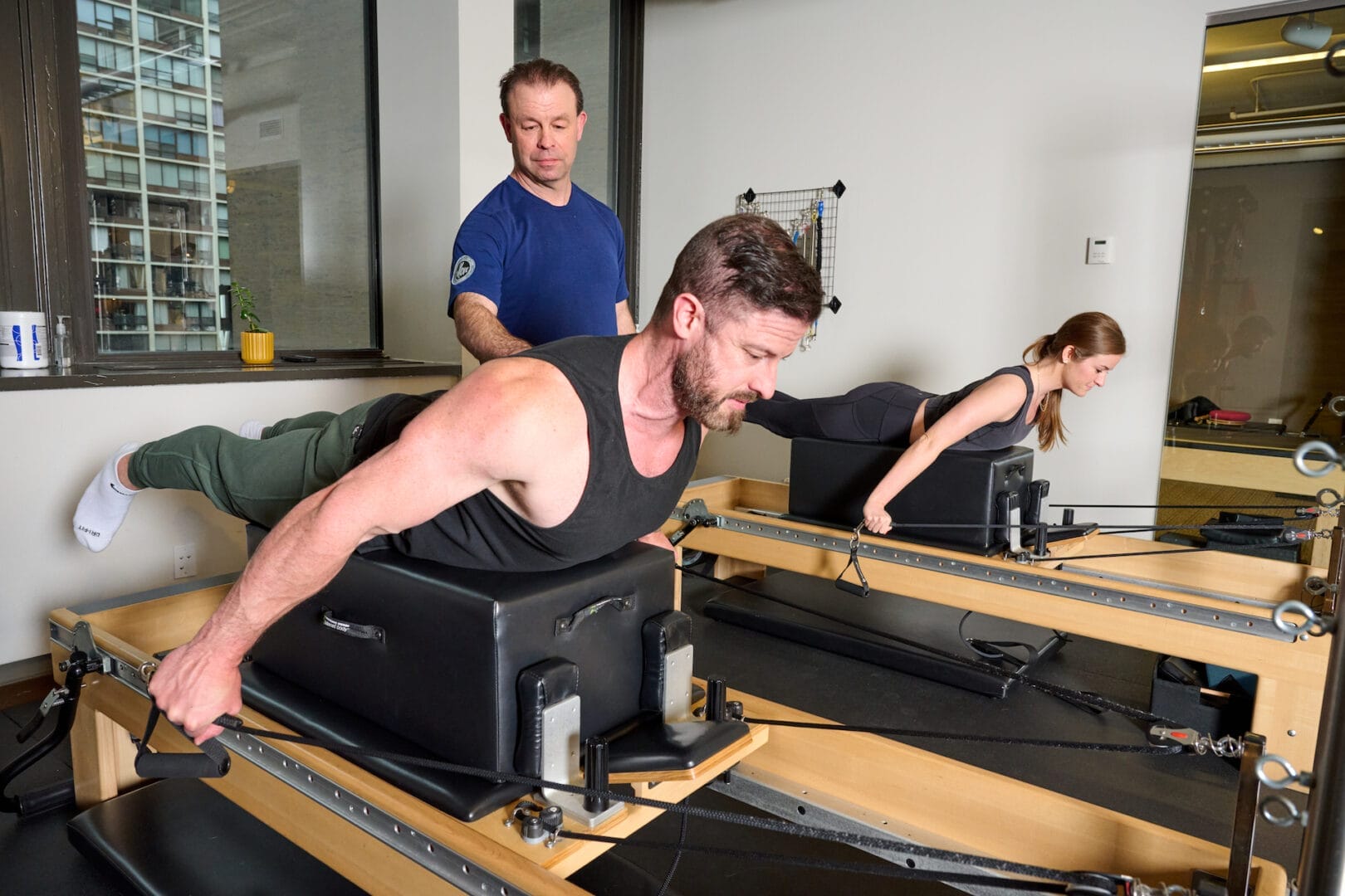 Two people use Pilates reformer machines, guided by an instructor, performing back extension exercises in a fitness studio specializing in Pilates for Rehab in Chicago.